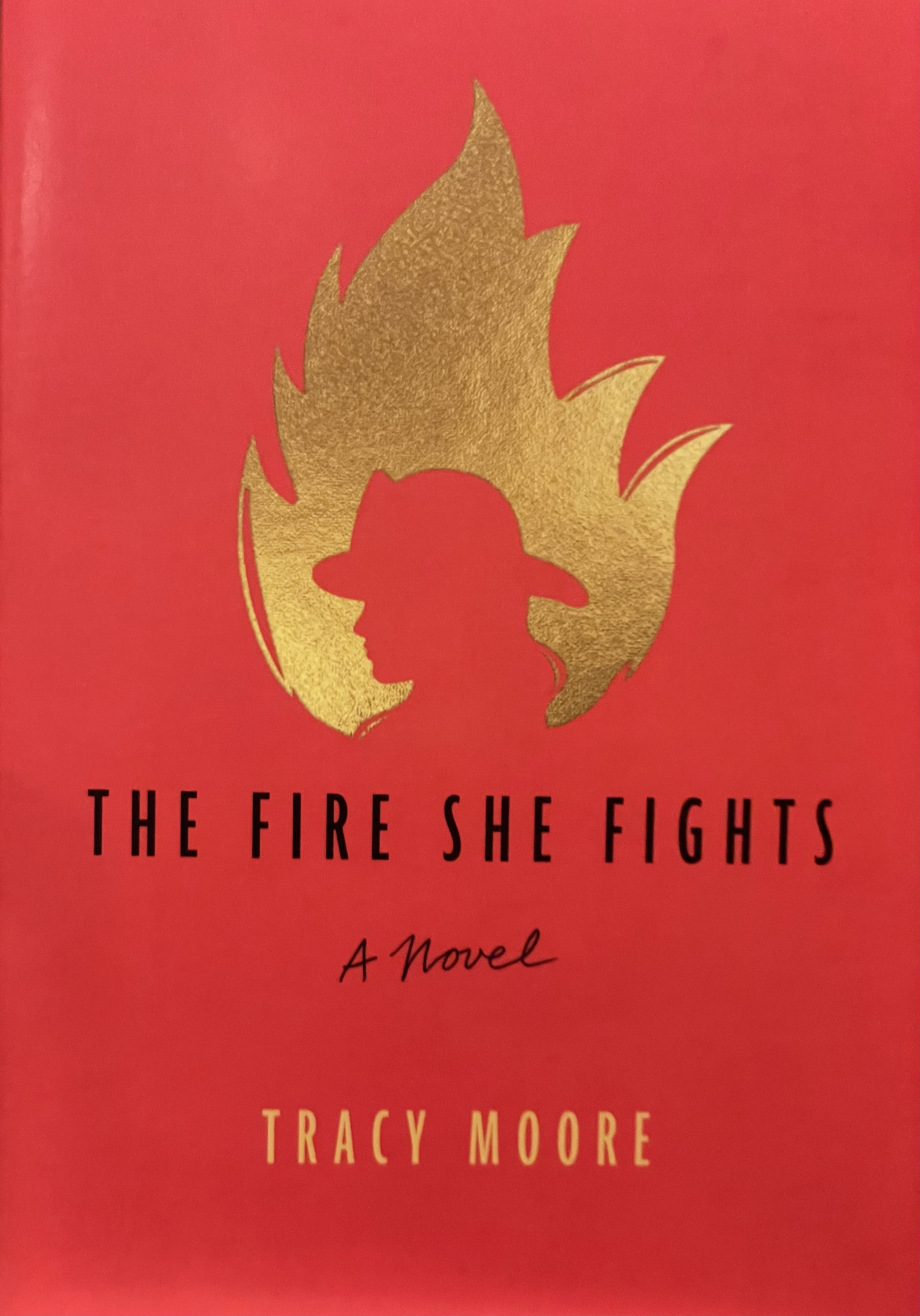 Cover of the novel The Fire She Fights. Red with a gold flame and a sillouette of a firefighters.